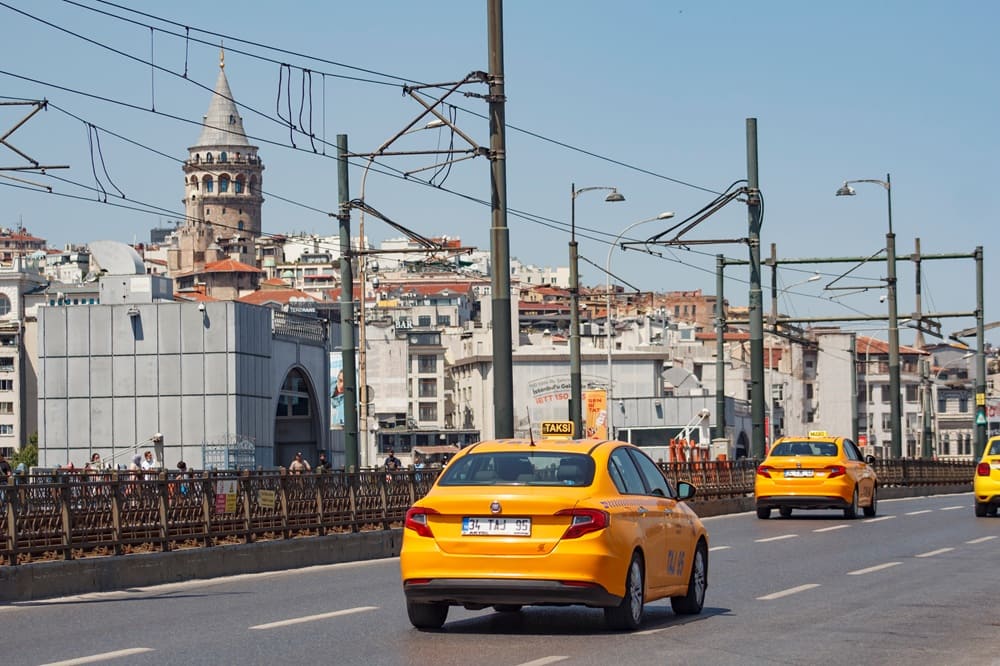 Yellow taxis driving across Galata Bridge with Galata Tower in the background, a common way for fans to travel in Istanbul during the 2026 UEFA Europa League Final